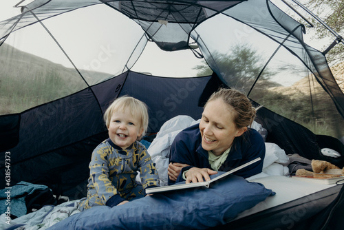 A mother reads a book to her young toddler son inside a tent during a camping trip in Oregon.