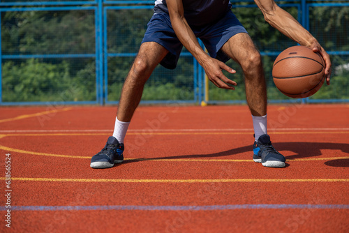 Muscular legs of unrecognizable basketball player training in outdoor court.