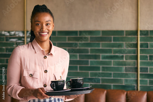 Portrait Of Smiling Female Owner Or Staff Member Carrying Cups In Cafe Or Coffee Shop