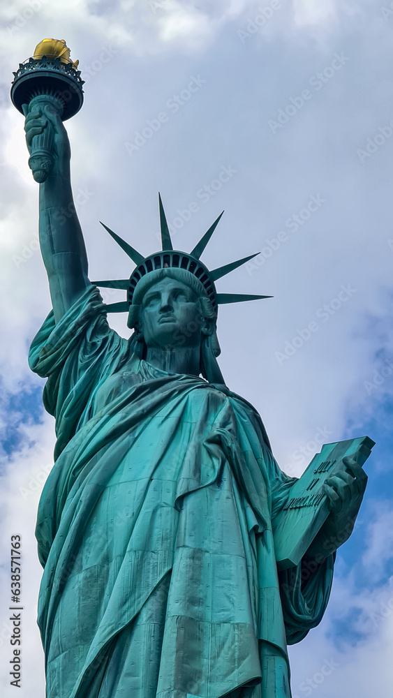 Fototapeta premium A close up on an iconic representation of freedom and independence, the Statue of Liberty with flaming torch on Liberty Island. The Lady on a Pedestal is surrounded by clouds. American history.