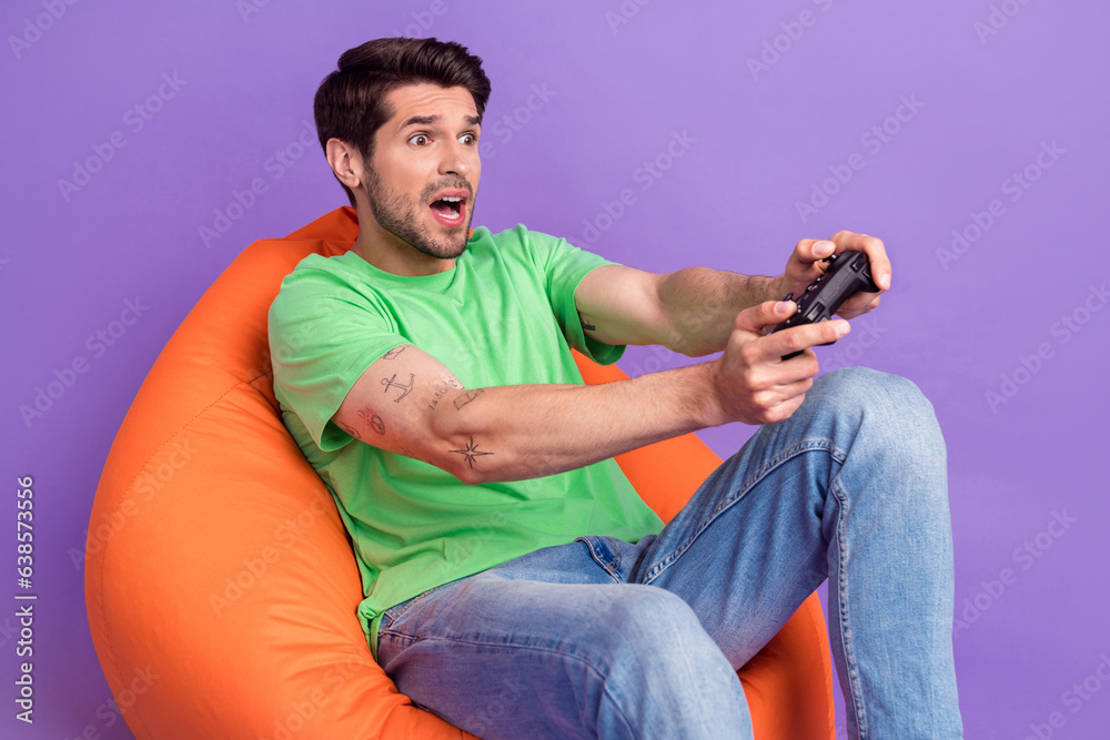 Photo of young funny staring man hold playstation gamepad console sitting pouf addicted losing isolated on violet color background Photo of young funny staring man hold playstation gamepad console sitting pouf addicted losing isolated on violet color background