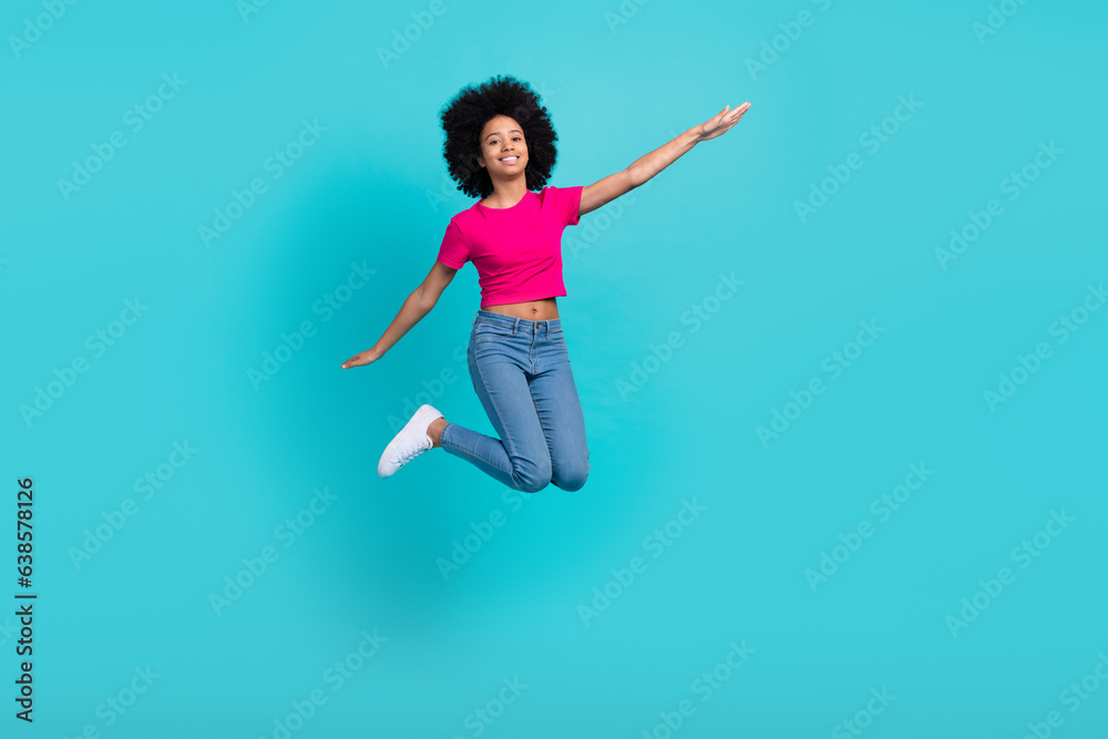 Full size photo of excited energetic small girl jumping arms wings flying have good mood isolated on teal color background
