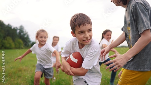a group of children run on the grass in the park with a ball. happy family childhood dream concept. children run on the green grass and play american football together. lifestyle kids have fun