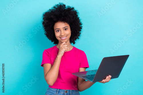 Portrait of intelligent kid with perming coiffure dressed stylish t-shirt hold laptop finger on chin isolated on blue color background © deagreez