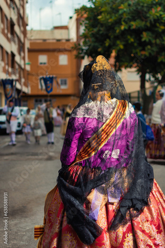 Woman, Fallera standing on the streets of Valencia, Spain, viewed from behind. She is wearing a traditional dress and her head is covered by a cloak photo