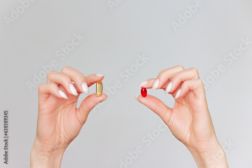 female hands holding yellow and red gel capsules with their fingers close-up on a light background photo