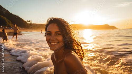 Une femme avec un grand sourire un en train de se baigner dans les vagues avec un coucher de soleil en arrière-plan.