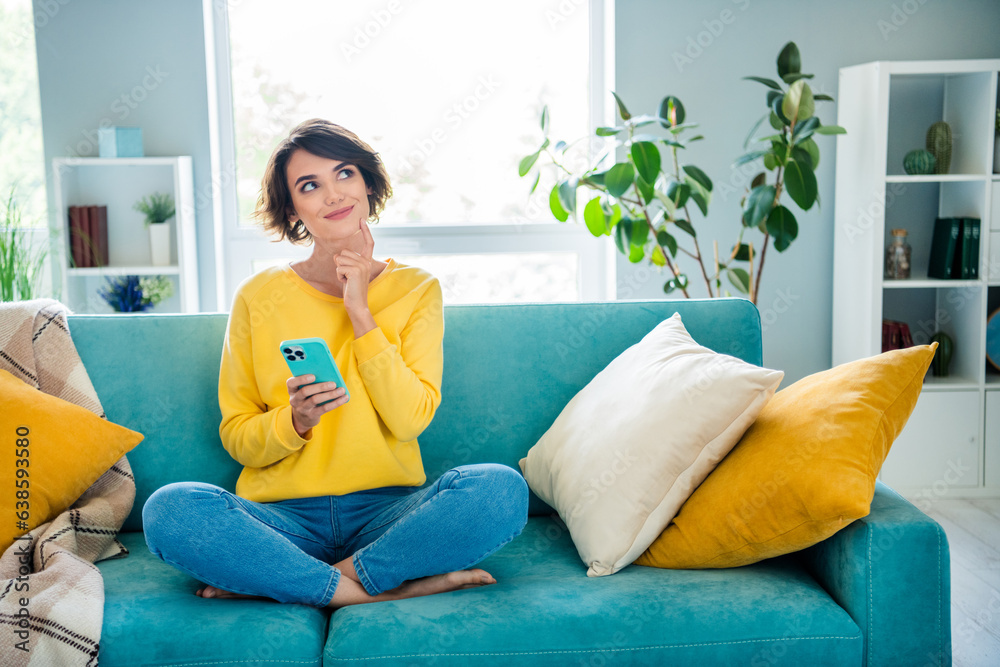 Portrait of pretty dreamy girl sitting on soft cozy couch use phone watching up planning weekend indoor house modern flat - obrazy, fototapety, plakaty 