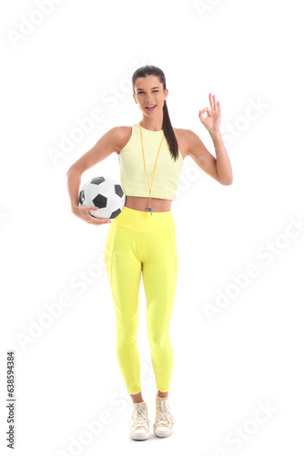 Sporty female coach with soccer ball showing OK on white background