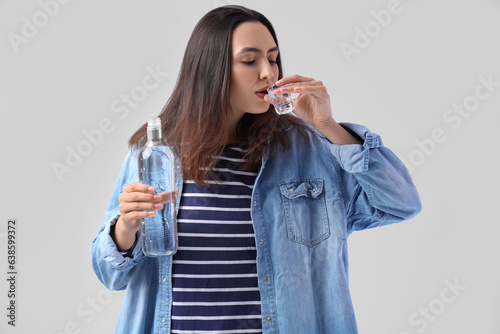 Young woman drinking vodka on light background