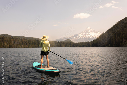 A young woman cools off in an alpine lake at the base of Mt. Hood with her standup paddle board on a summer day. 