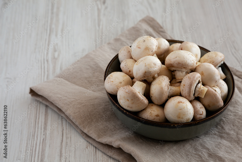 Raw White Champignon Mushrooms in a Bowl on a white wooden background, side view. Copy space. Raw White Champignon Mushrooms in a Bowl on a white wooden background, side view. Copy space.