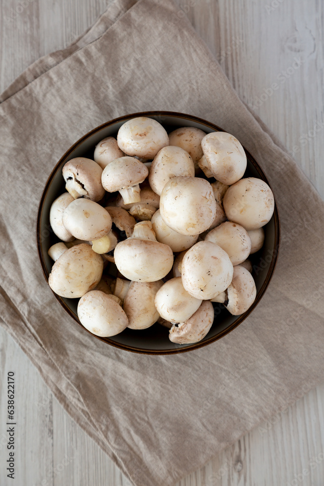 Raw White Champignon Mushrooms in a Bowl on a white wooden background, top view. Overhead, from above, flat lay. Raw White Champignon Mushrooms in a Bowl on a white wooden background, top view. Overhead, from above, flat lay.