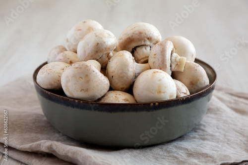 Raw White Champignon Mushrooms in a Bowl on a white wooden background, side view. Close-up.