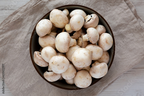 Raw White Champignon Mushrooms in a Bowl on a white wooden background, top view. Overhead, from above, flat lay.