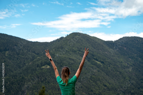 Woman with raised arms standing under blue sky with mountain view