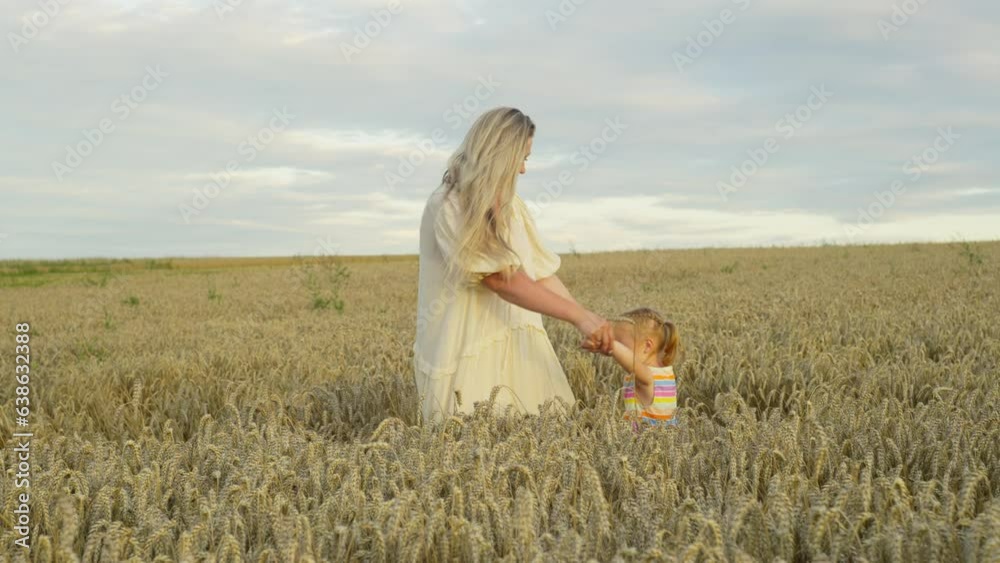 mother holding her daughter's hands and dancing in a wheat field. The concept of happiness, smiles, parental love, happy carefree childhood. Cultivation of cereals on agricultural fields. mother holding her daughter's hands and dancing in a wheat field. The concept of happiness, smiles, parental love, happy carefree childhood. Cultivation of cereals on agricultural fields.