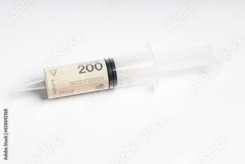 A large syringe and a Polish banknote of PLN 200 lying on a white background (selective focus)