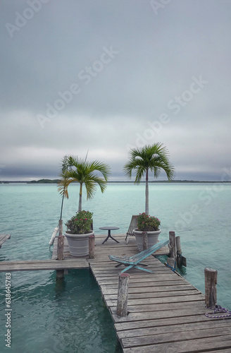 a wooden sun lounger with a palm tree on the pier of a Mexican freshwater lake. lagoon 7 colors, bacalar. pleasant overcast maximum lounge atmosphere. vertical photo © Dmytro