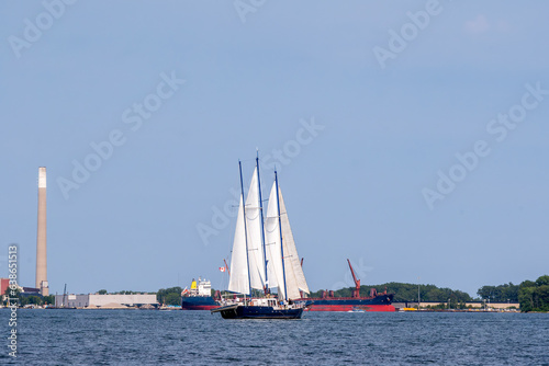 a sail boat travels across toronto s inner harbour with a laker  commercial shipping vessel  tied-up in the background  shot in summer room for text