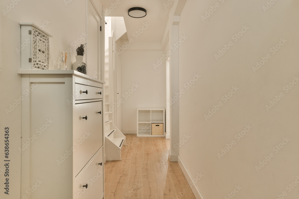 a long narrow room with white walls and wood flooring on the right side, there is an open door leading to another room a long narrow room with white walls and wood flooring on the right side, there is an open door leading to another room