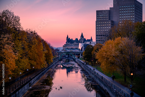 Fall foliage around the Rideau Canal, with the exterior of the landmark hotel Fairmont Chateau Laurier and pink sunset sky. Autumn view of downtown Ottawa, Ontario, Canada, November 2021.