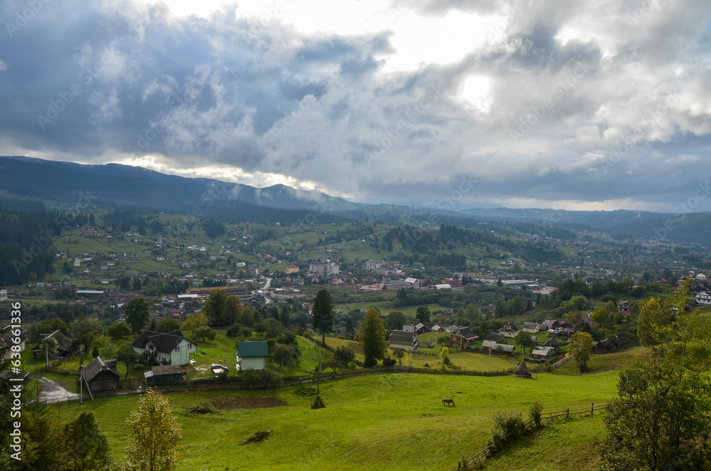 Panoramic view of mountain village Vorokhta. Rural landscape with green field, trees, houses and mountains on background. Carpathian Mountains, Ukraine.