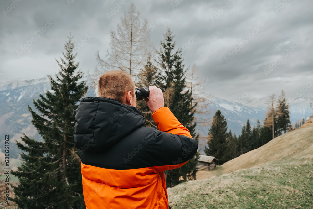 Viewing with binoculars.Hiking in the mountains in the spring season.Man with binoculars. man in a warm jacket looks through binoculars at a mountain landscape. walking in the mountains Viewing with binoculars.Hiking in the mountains in the spring season.Man with binoculars. man in a warm jacket looks through binoculars at a mountain landscape. walking in the mountains