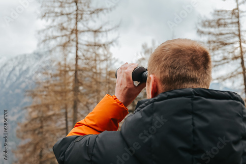 Viewing the mountains with binoculars.Hiking in the mountains in the spring season.Man with binoculars. man in a warm jacket looks through binoculars at a mountain landscape. walking in the mountains
