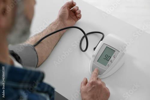 Man measuring blood pressure at table indoors, closeup photo