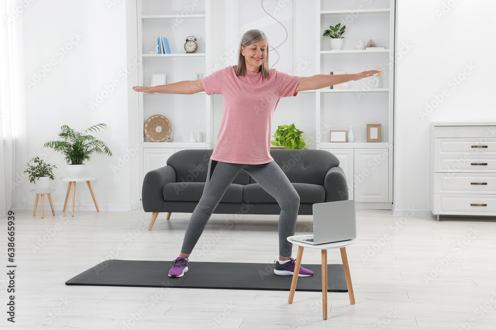 Senior woman in sportswear doing exercises near laptop at home