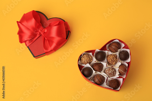 Heart shaped box with delicious chocolate candies on yellow background, flat lay