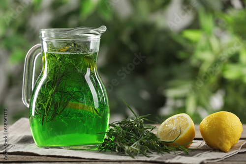 Jug of refreshing tarragon drink with lemon on table, space for text