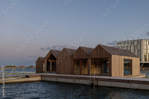 Outdoor exterior view at waterfront of Nordhavn Bassin, wooden floating public bath, Strandbad Nordhavn, and UN City building during sunset time in Copenhagen, Denmark.
