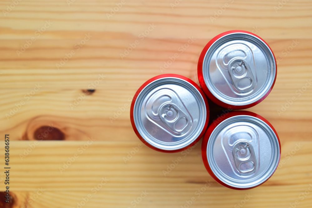 three aluminium red cans of soft drink put on brown wooden table