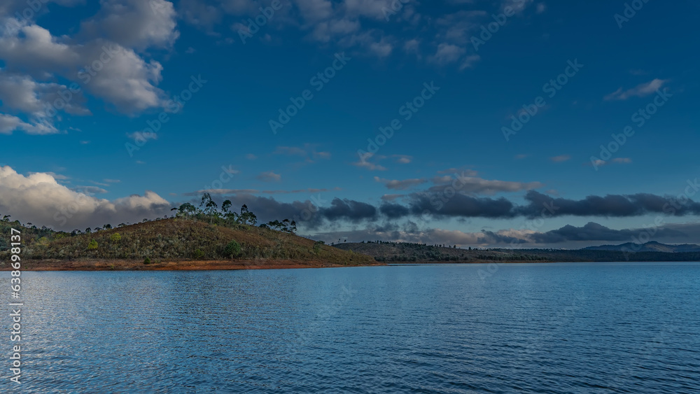Beautiful blue lake. Coastal hills with green vegetation against the sky and clouds. Ripples on calm water.  Madagascar. Mantasoa Lake.