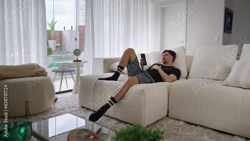 Sleepy young man brownsing on his phone until he falls asleep. Man lying on the couch at home on a lazy morning