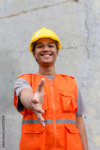 Young Asian worker wearing orange vest and safety helmet smiling friendly offering handshake for business