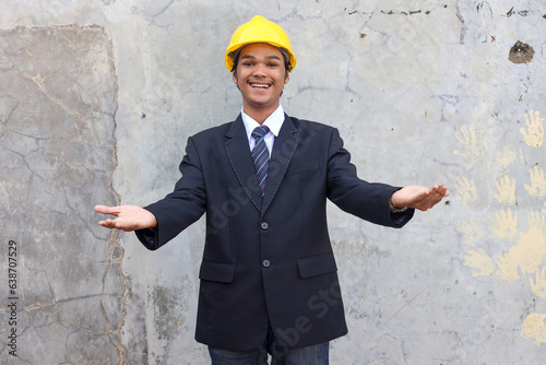 Cheerful Asian male manager in formal clothes and safety helmet showing welcoming gesture