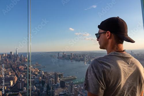 A man in sunglasses enjoying the view of New York City skyline over the Hudson River during the dusk from The Edge. Clear sky. Endless rows of tall buildings. Bustling and lively city. Freedom
