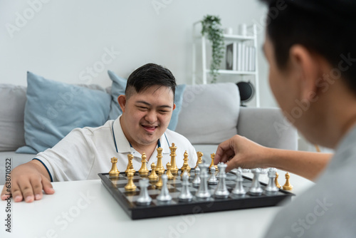 Asian attractive father playing chess game with his son in living room. 