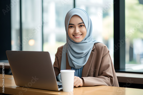 Portrait of young muslim woman wearing hijab working with laptop computer in her modern business office. photo