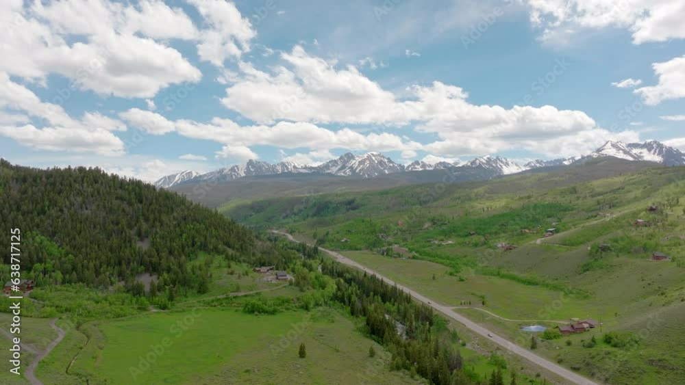 Aerial view of beautiful Colorado mountain range with snow capped peaks on a sunny, blue sky day in the summer with green fields, trees, and mountain homes Aerial view of beautiful Colorado mountain range with snow capped peaks on a sunny, blue sky day in the summer with green fields, trees, and mountain homes