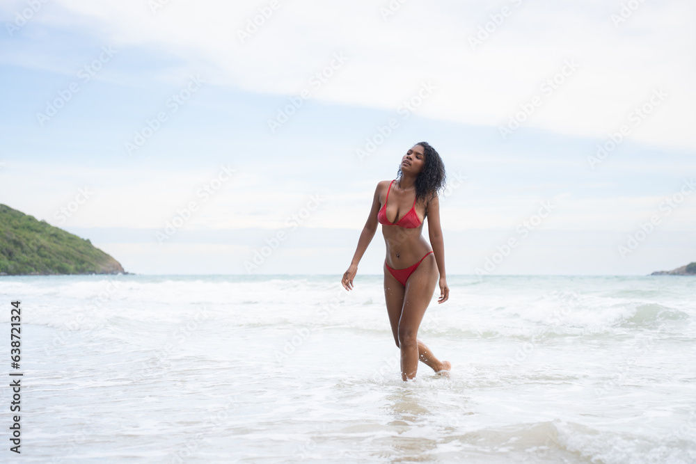 Portrait of happy young woman in red bikini walking on the beach.