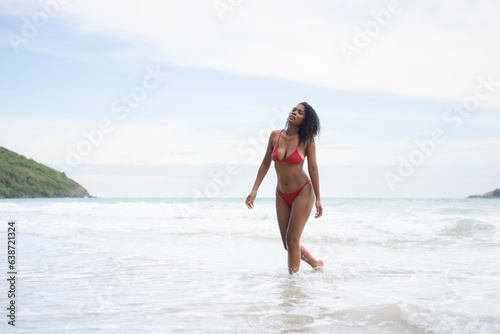 Portrait of happy young woman in red bikini walking on the beach.