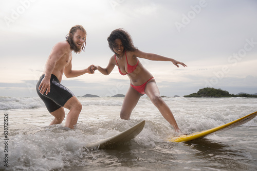 Couple surfing on the beach having fun and balancing on the surfboard