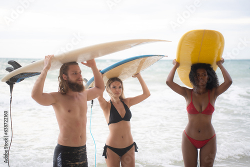Rear view of two women and young man holding surfboards on their heads and walk into the sea to surf