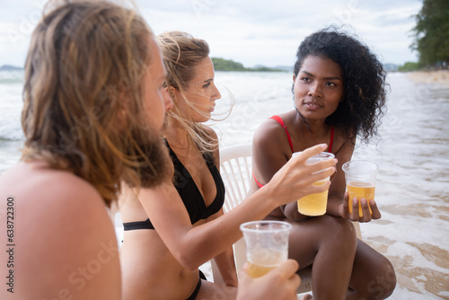 Multi-ethnic group of friends sitting on chairs with drinks on the beach