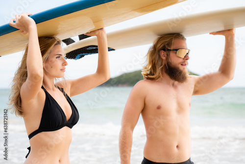Young man and woman holding surfboards on their heads and walk into the sea to surf