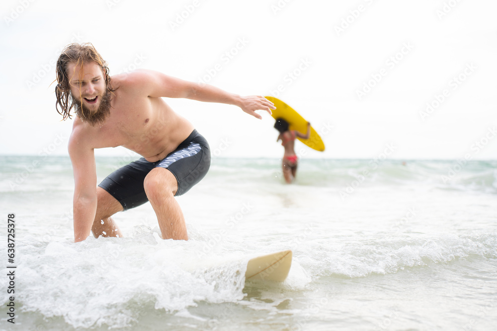 Fototapeta premium Young man surfing on the beach having fun and balancing on the surfboard